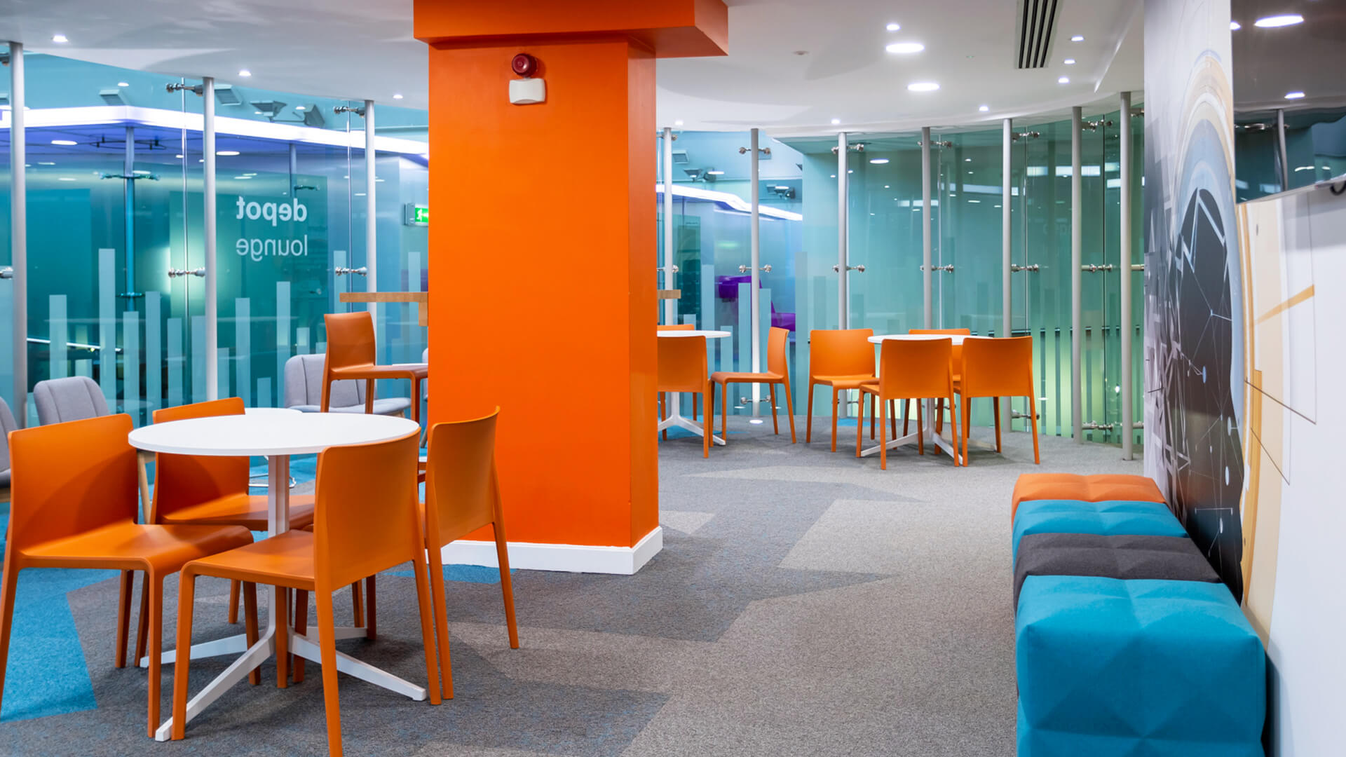 Orange chairs surround circular tables in the glass-walled Digital Depot lounge