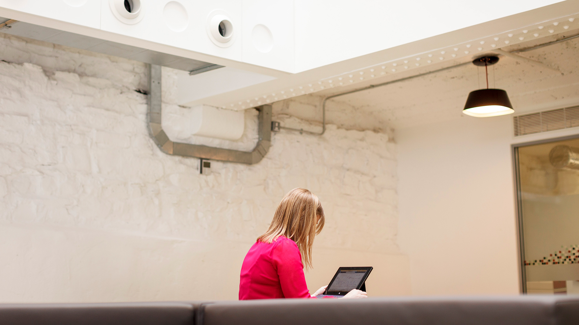 A woman in a pink top works at a digital tablet in a white meeting room in the Grainstore building