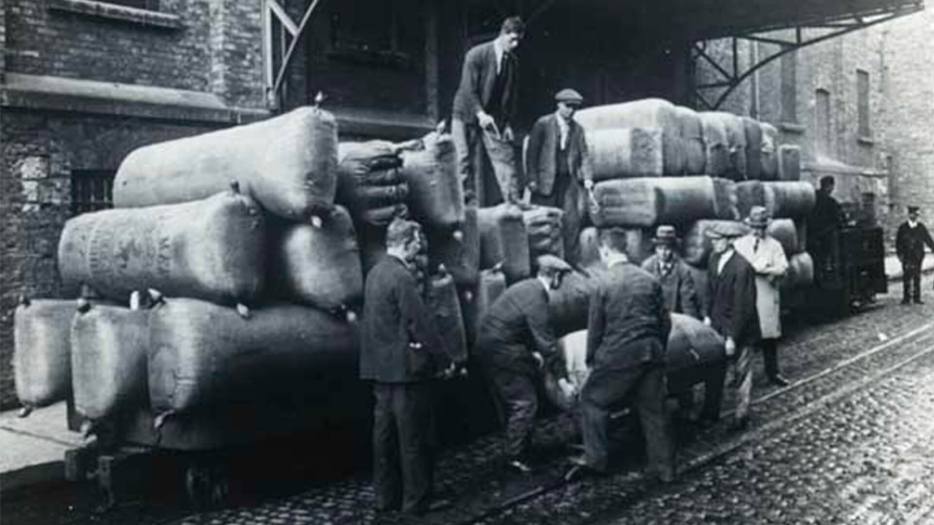 A black-and-white historical shot of men unloading the hop wagons at the Guinness Brewery