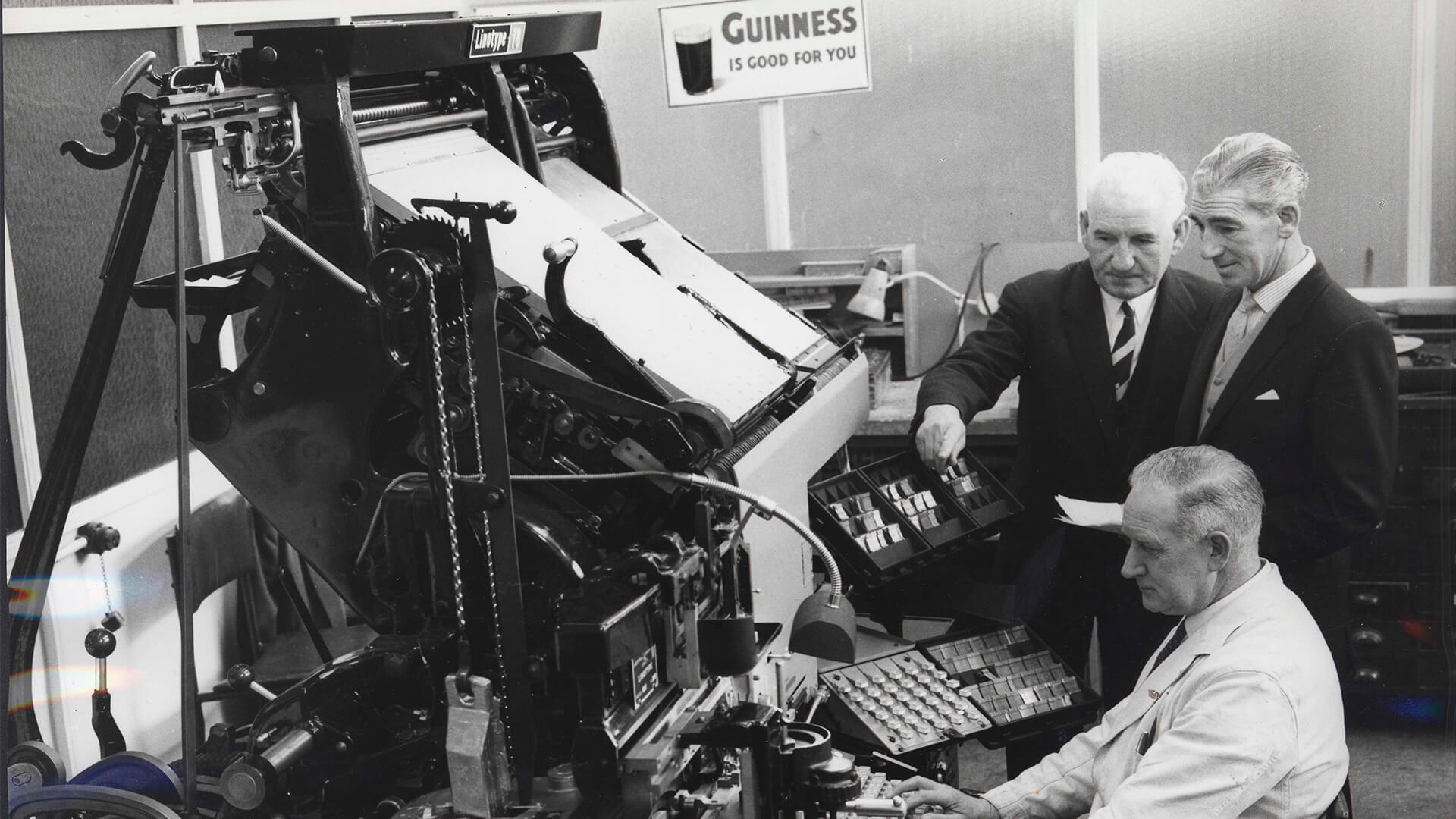 A black-and-white historical shot shows three men working on the Guinness Printworks Linotype Machine